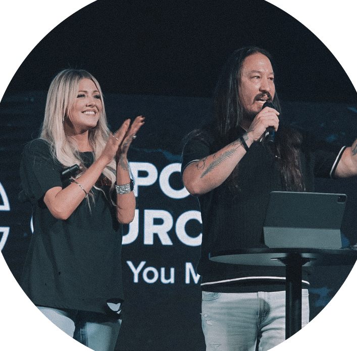 A man with long hair speaks at a podium while a woman with long hair stands beside him, both smiling and clapping. They are in front of a screen displaying the words "You Matter" and the logo of a church.