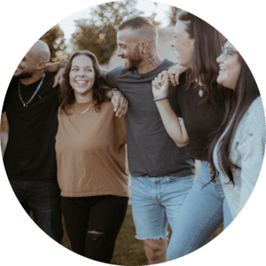 A group of five individuals standing closely together outdoors. They are smiling and wearing casual clothing, with a mix of dark and light colors. The background features trees, and the atmosphere looks relaxed and friendly.