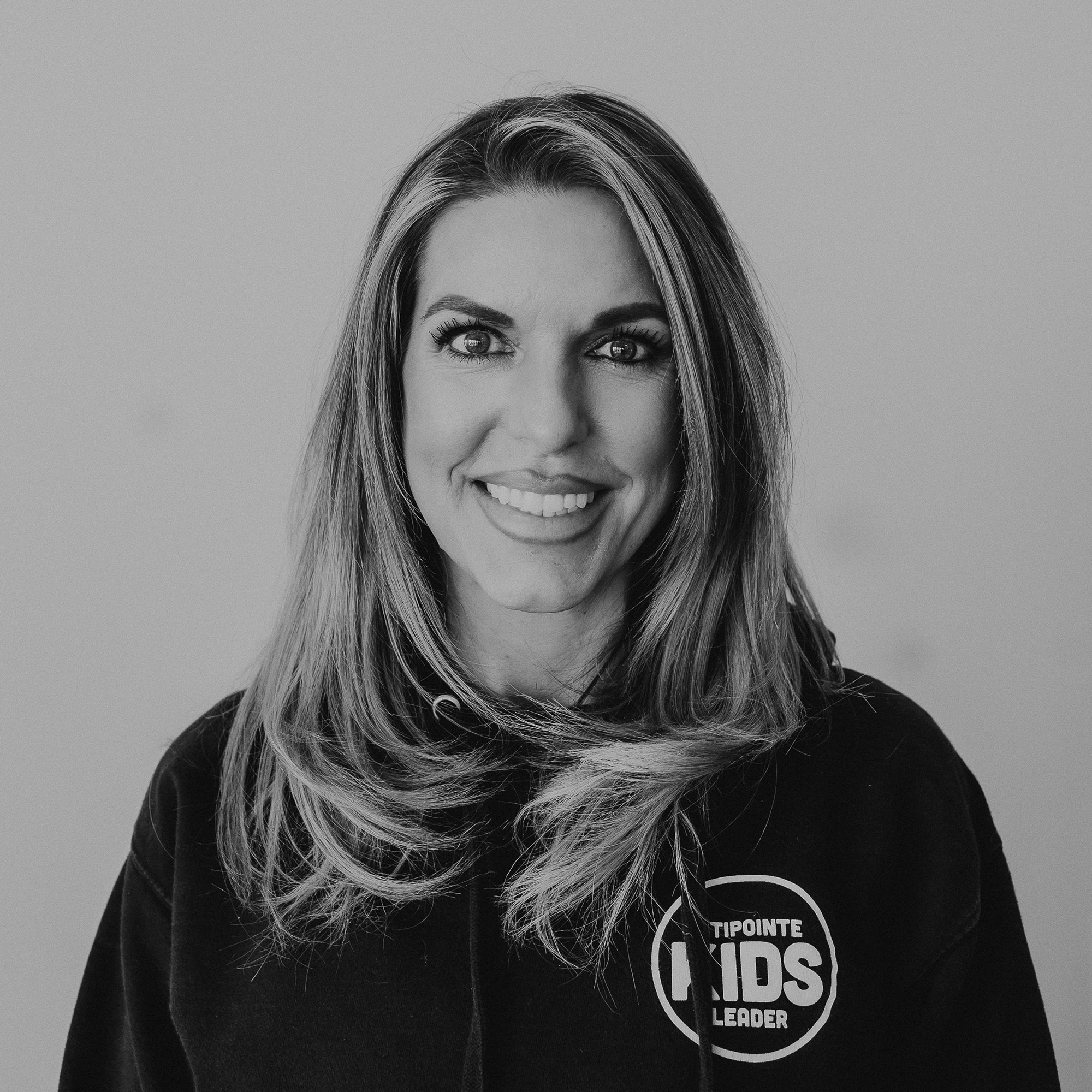 A woman with long, wavy hair wearing a black hoodie with the text 'TipiPointe Kids Leader' displayed prominently. She is smiling and facing the camera against a neutral background.